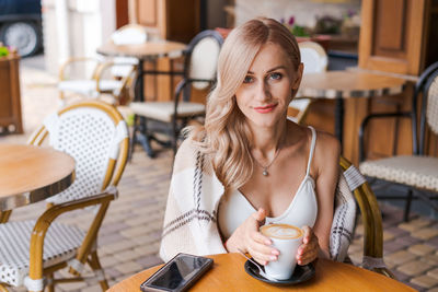 Young beautiful woman, in cafe, drinking coffee in cup, in cozy plaid happy