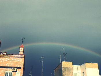 Low angle view of rainbow over buildings against sky