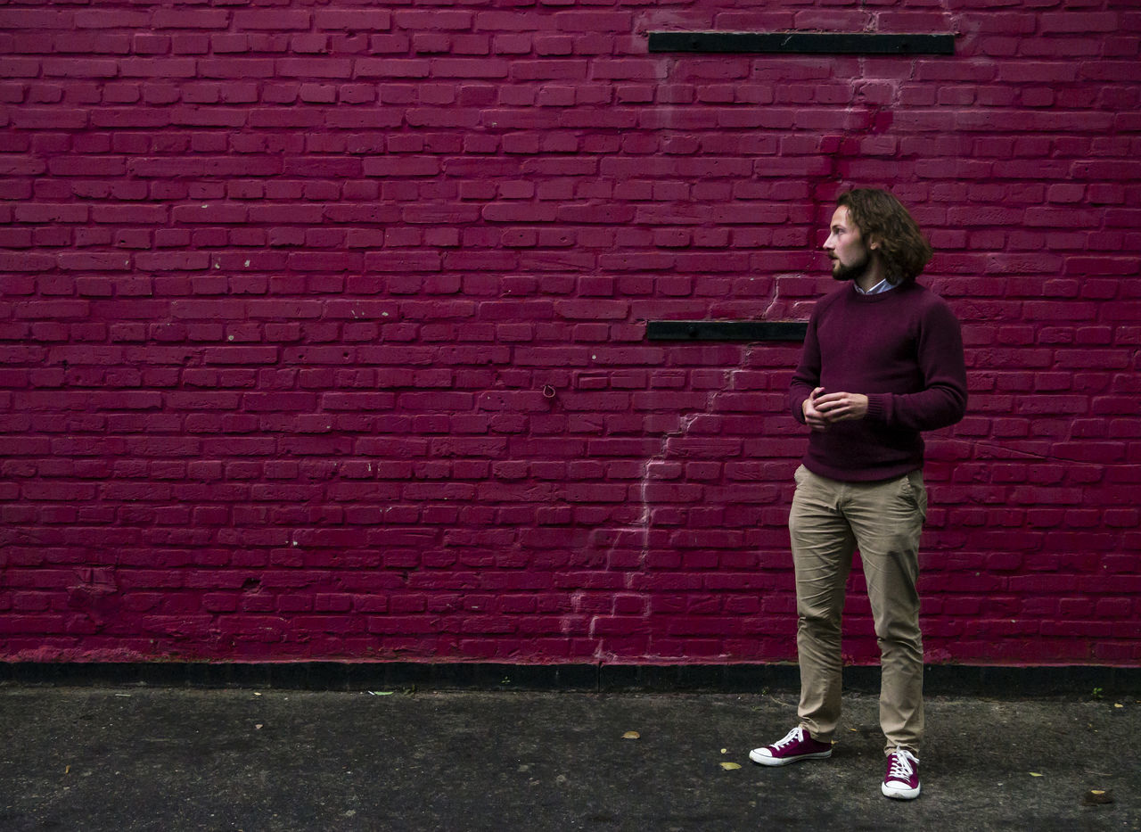 Young man standing against brick wall