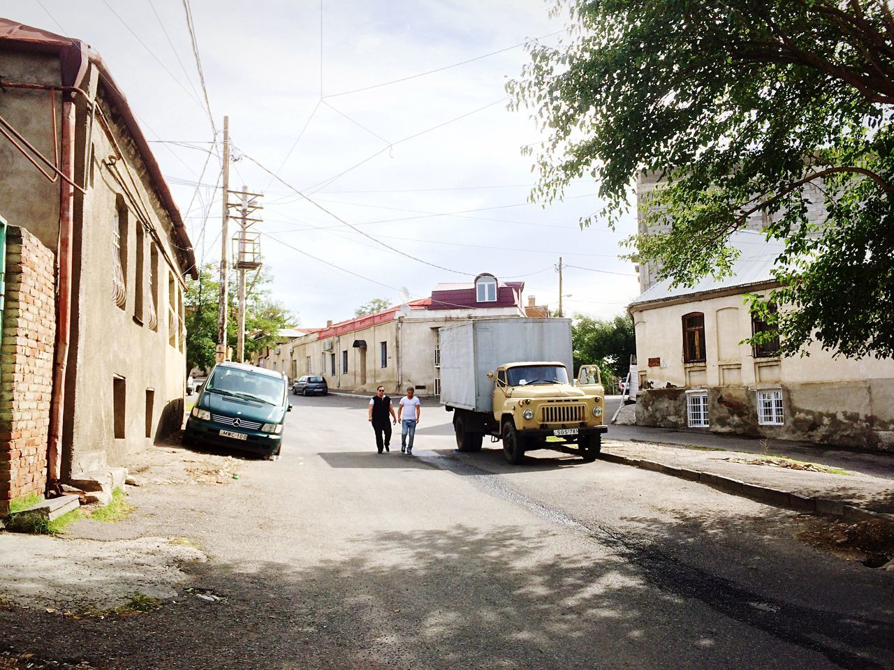 building exterior, mode of transport, transportation, built structure, land vehicle, architecture, car, street, road, tree, city, sky, residential building, travel, zebra crossing, roadside, person, day, outdoors, growth, power line