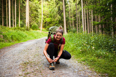 Portrait of woman tying shoelace on road in forest