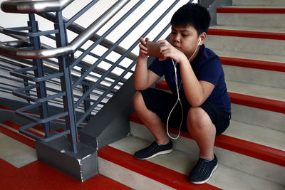 Full length of boy sitting on mobile phone