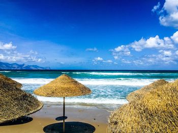 Thatched roof parasols at beach against blue sky