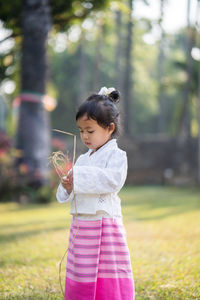 Girl holding hay while standing on grass at garden against trees