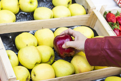 Cropped hand of woman picking red apple from container at market stall