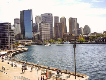 Modern buildings by river in city against sky