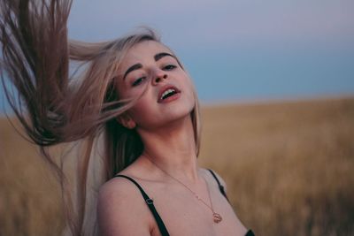 Beautiful woman tossing hair on field against sky