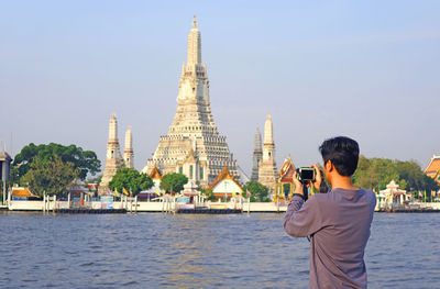 Man taking photos of the temple of dawn, the landmark on chao phraya river bank, bangkok, thailand