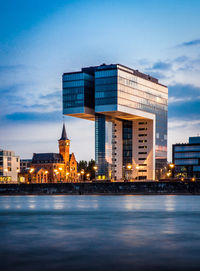 Modern buildings by sea against sky in city at dusk