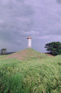 Lighthouse on field by building against sky