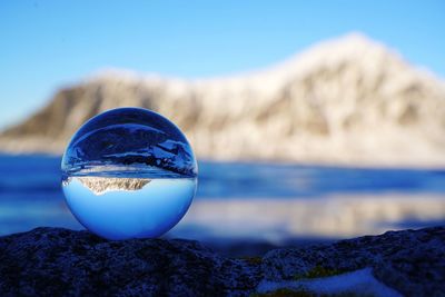 Close-up of crystal ball on rock against blue sky