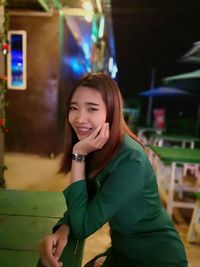 Portrait of smiling young woman sitting at outdoor cafe during night