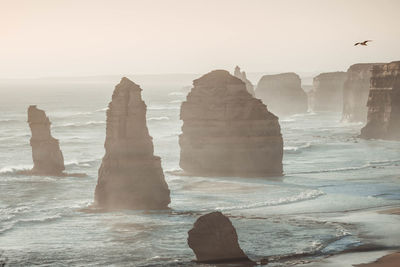 The twelve apostles in sea against clear sky during foggy weather
