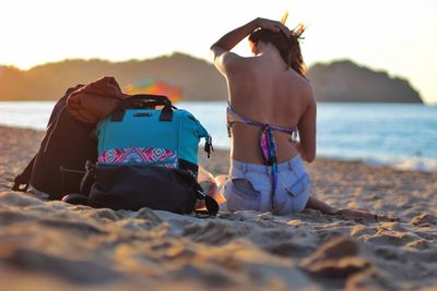 Rear view of woman by bags sitting on sandy beach