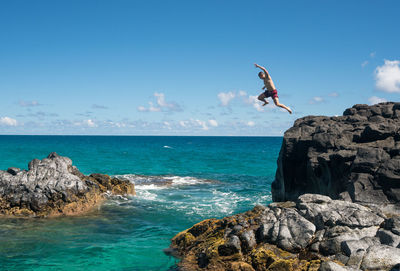 People jumping on rock by sea against sky