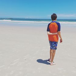 Rear view of teenager boy standing at beach against sky