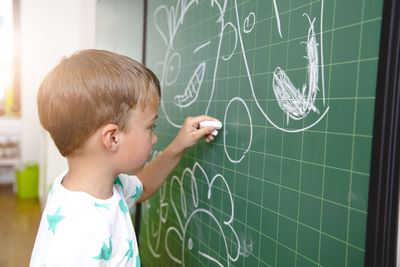 Side view of boy writing on blackboard