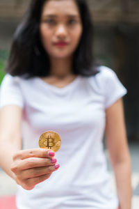 Portrait of young woman holding bitcoin while standing outdoors