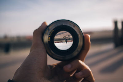 Cropped image of person holding camera lens at beach