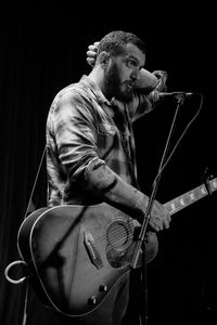 Man with guitar standing against black background