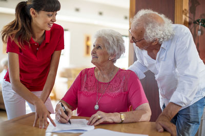 Senior woman signing a contract, nurse and senior man helping her