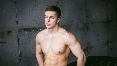 Shirtless muscular man standing by wall