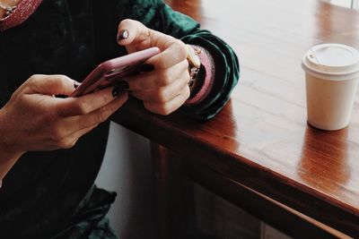 Midsection of woman using mobile phone at table