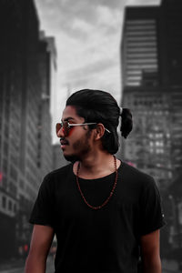 Young man wearing sunglasses looking away while standing outdoors