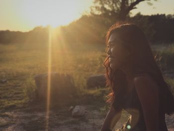 Side view of young woman standing against trees at sunset