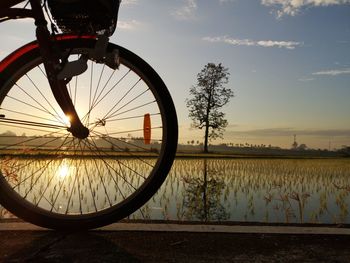 Bicycle wheel on field against sky at sunset