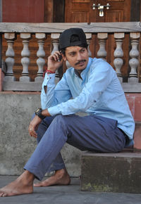 Side view of a young guy touching his cap with looking sideways while sitting on the temple stairs