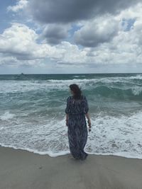 Rear view of woman standing on beach against sky