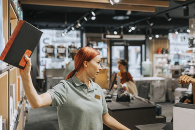 Redhead female sales clerk removing appliance from rack at electronics store