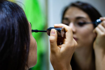 Close-up of woman applying mascara against mirror