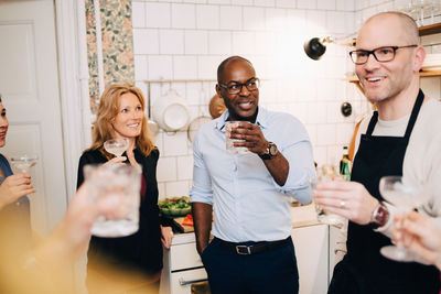 Multi-ethnic mature friends enjoying drinks while talking in kitchen at home