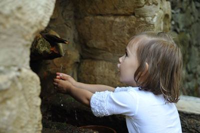 Side view of girl washing hands at faucet outdoors