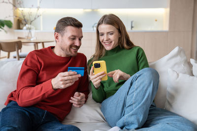 Happy wife and husband spending money in online shops using smartphone with credit card at home