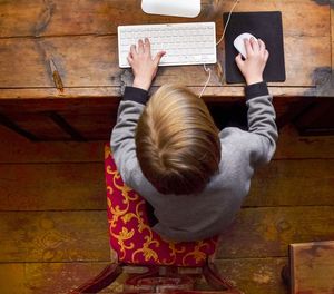 High angle view of kid sitting near table, working with computer