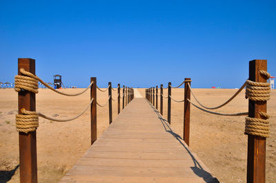 View of wooden walkway against clear blue sky