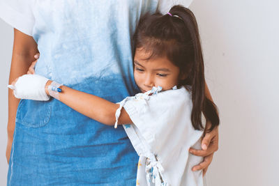 Girl embracing mother against wall in hospital