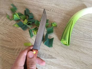 Cropped image of man holding knife by leek on wooden table