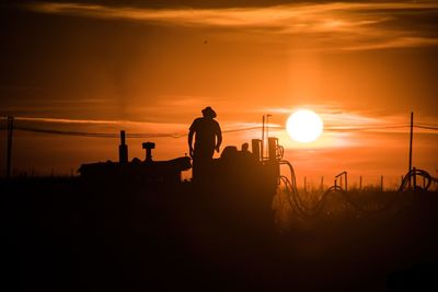 Silhouette man on tractor in field during sunset