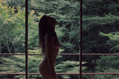 Side view of naked woman standing against trees