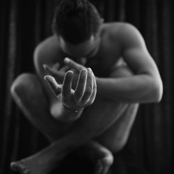 Naked man gesturing while sitting against wall