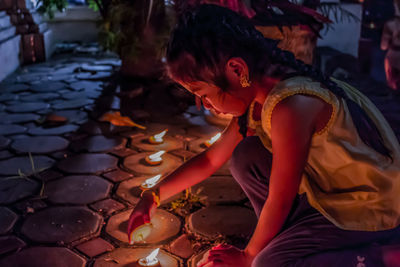 Cute girl lighting diya on footpath at night