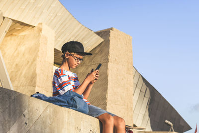 Boy using phone while sitting outside building