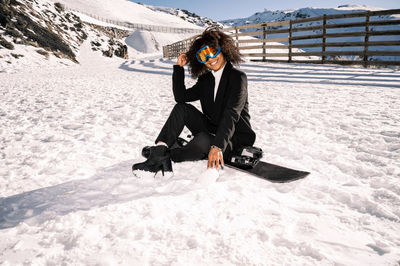 African american woman with goggles and a snowboard on a snowy mountain during winter