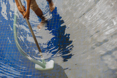 Low section of man cleaning swimming pool with vacuum cleaner