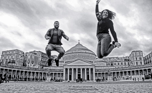 Low angle view of woman jumping against sky in city