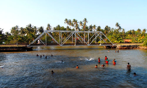 People on bridge over river against clear sky